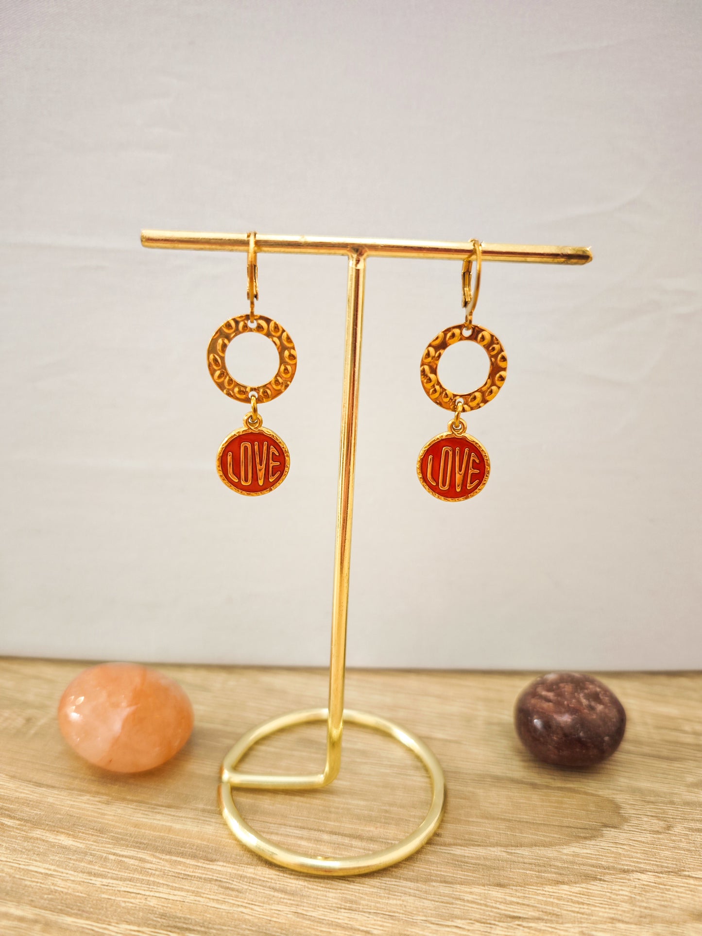 Boucles d’oreilles LOVE rouges et dorées en acier inoxydable doré présentées sur un support doré.