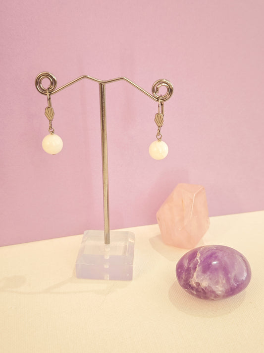 Boucles d’oreilles artisanales en acier inoxydable avec perles de nacre blanche, création Julie Gassmann sur fond rose et beige.