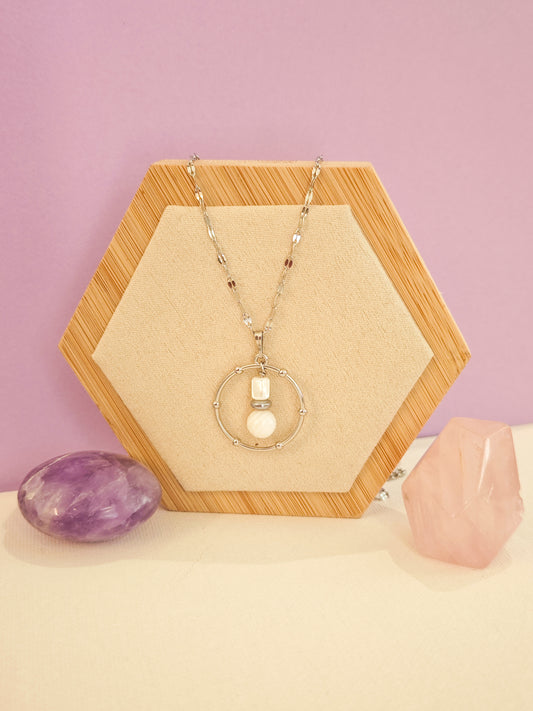 Collier artisanal en acier inoxydable avec pendentif cercle, nacre blanche et hématite, création Julie Gassmann sur fond beige et rose.