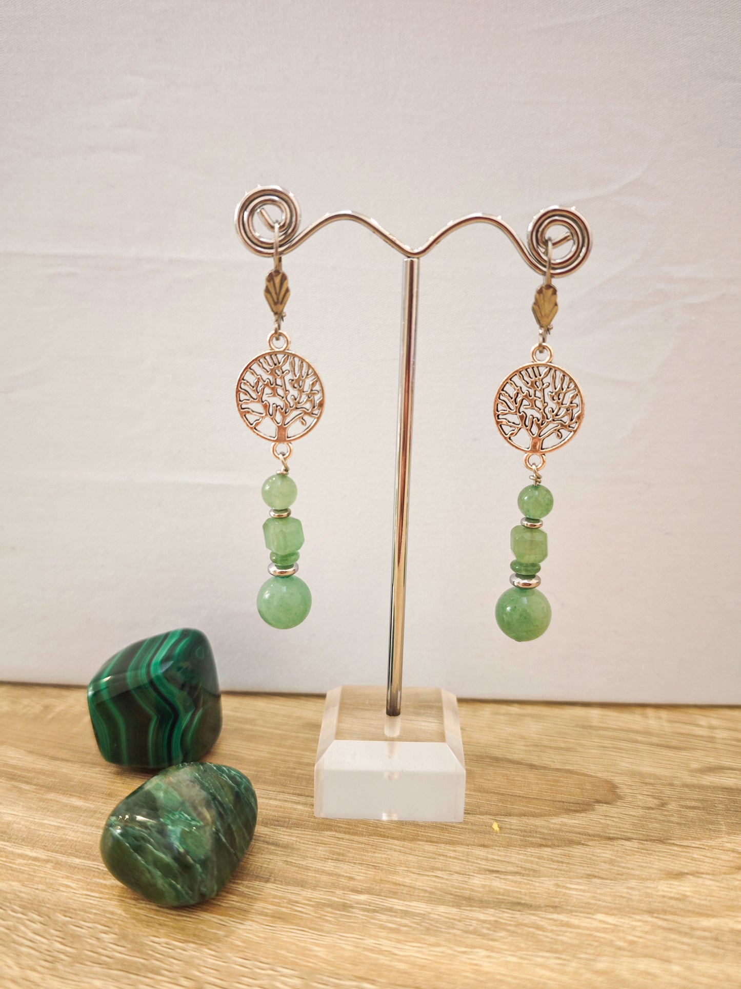 Boucles d’oreilles en acier inoxydable avec aventurine verte et hématite sur présentoir métallique, ambiance artisanale naturelle et élégante.