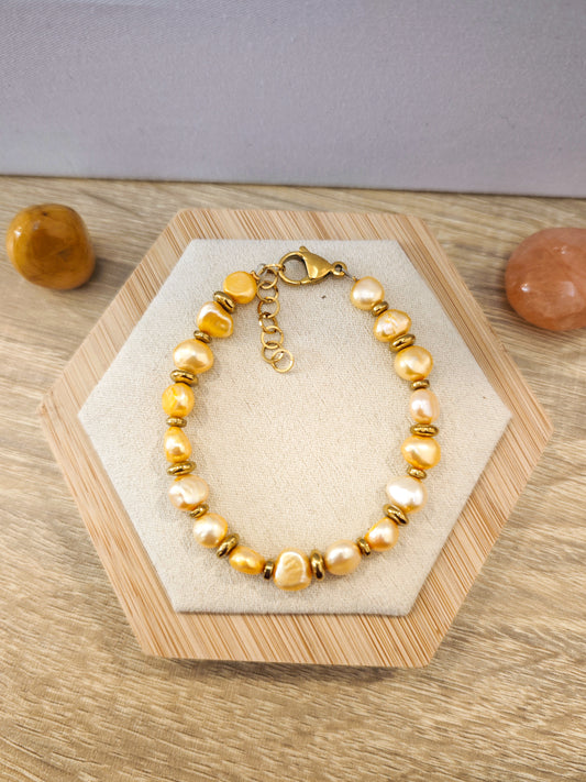 Bracelet artisanal en perles de culture jaunes et hématite dorée avec acier inoxydable doré présenté sur un support beige en bois.