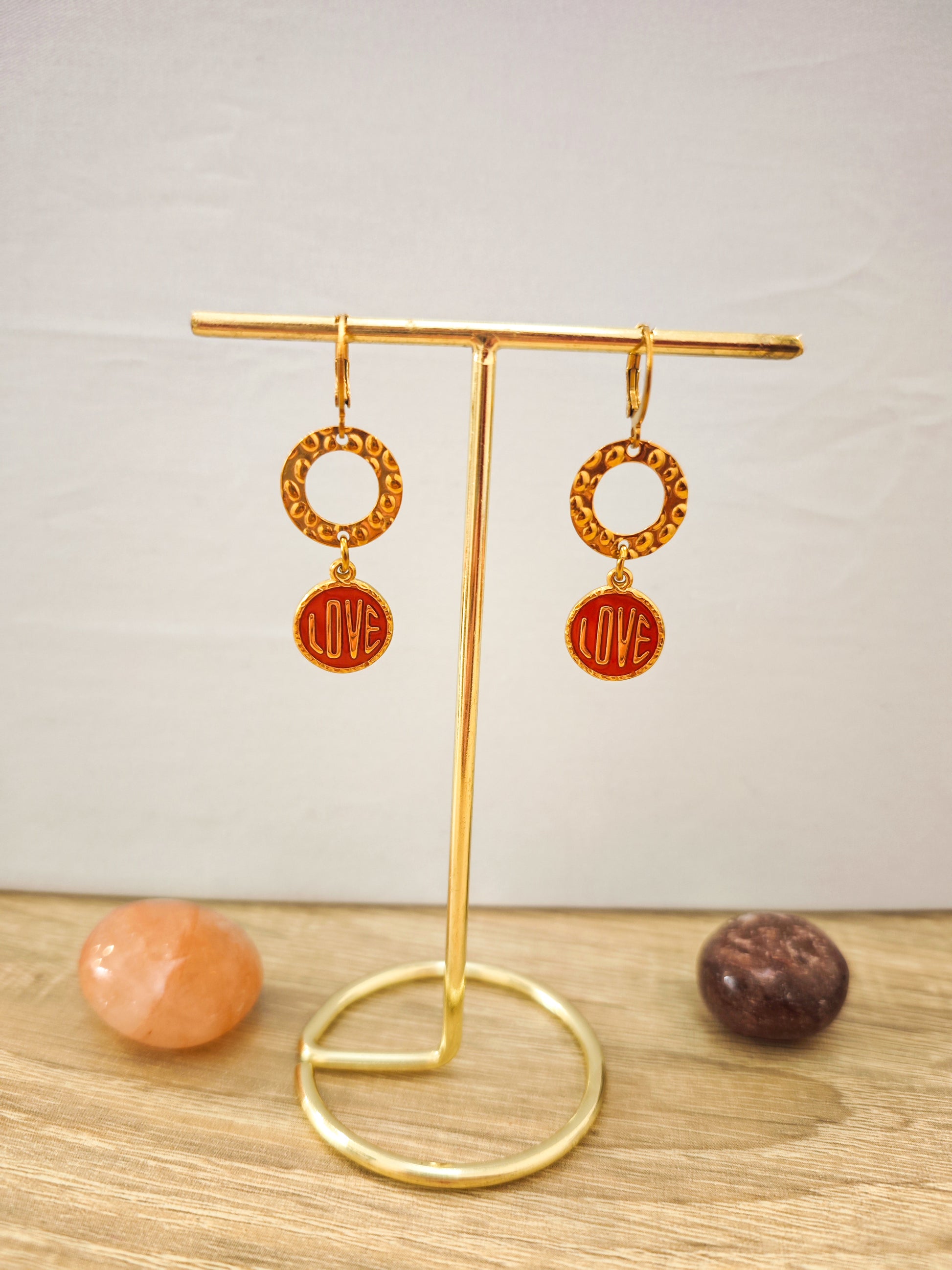 Boucles d’oreilles LOVE rouges et dorées en acier inoxydable doré présentées sur un support doré.