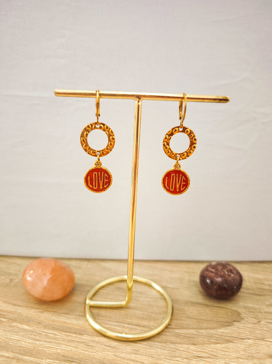 Boucles d’oreilles LOVE rouges et dorées en acier inoxydable doré présentées sur un support doré.