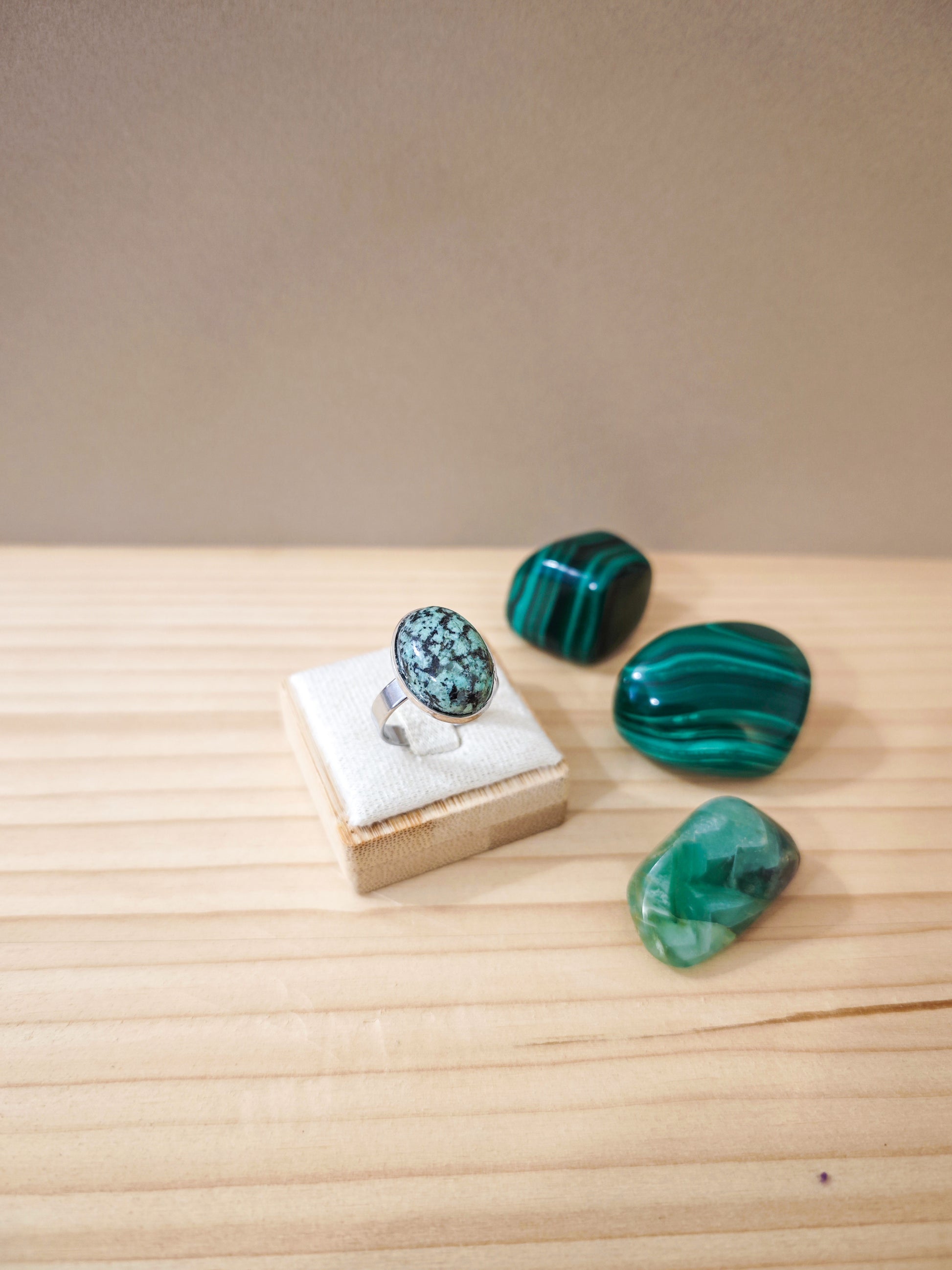 Bague artisanale en jaspe africain vert marbré montée sur acier inoxydable, pièce unique créée à la main à Nogent-sur-Marne, posée sur présentoir beige.